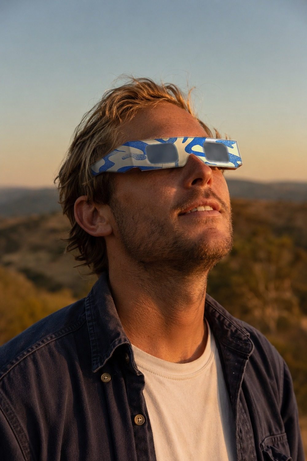 Person watching the sun through certified paper eclipse glasses with the blue Tide wave print at golden hour