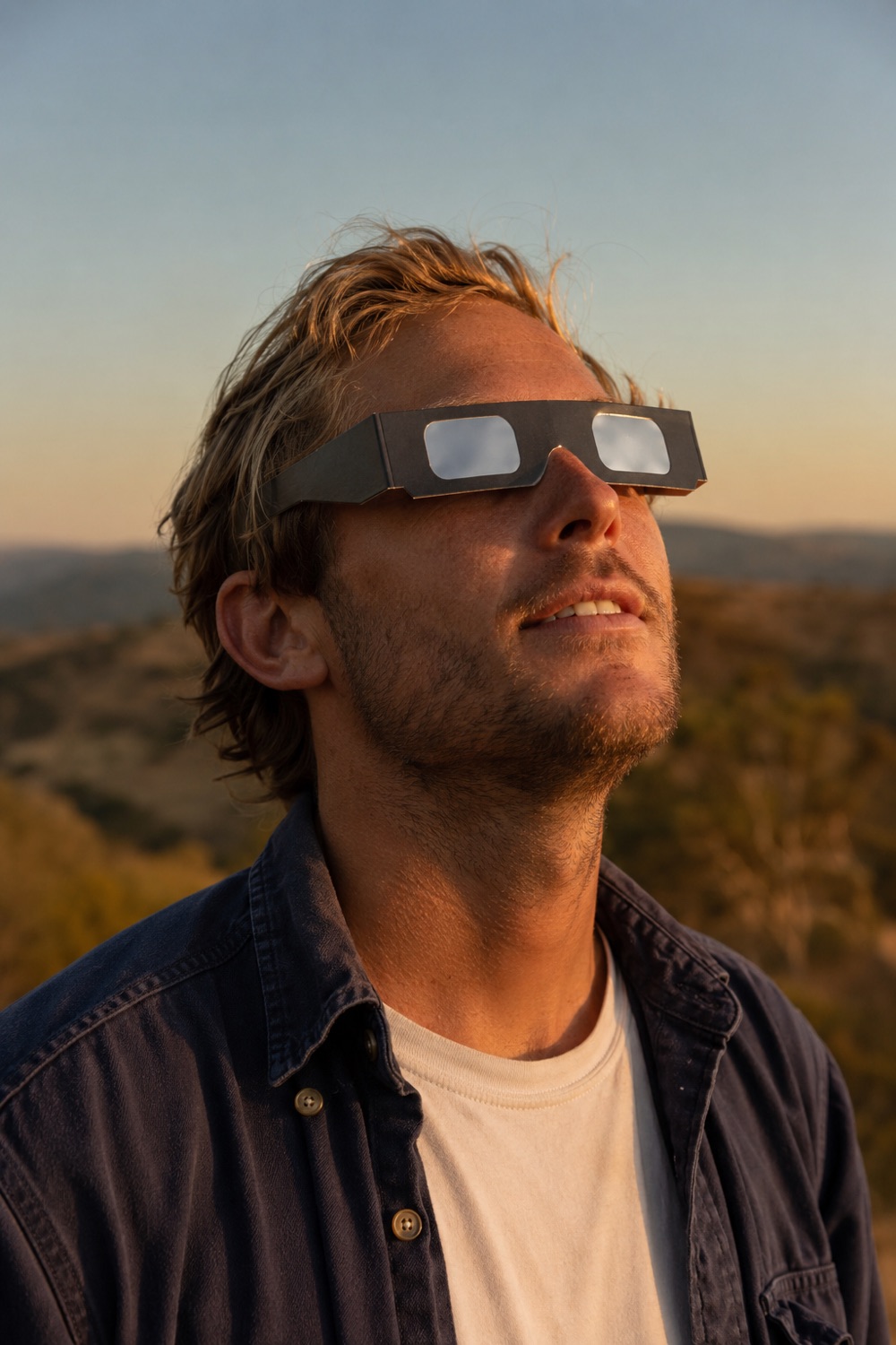 Person watching the sun through certified paper eclipse glasses at golden hour